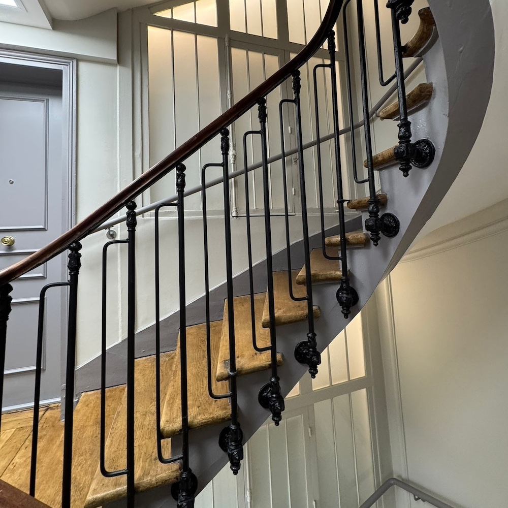 Cage d'escalier restaurée : marches en bois poncées, ferronnerie repeinte en noir, main courante vernie