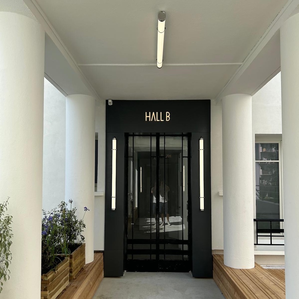 Hall d'immeuble rénové : porte vitrée noire, appliques, colonnes repeintes